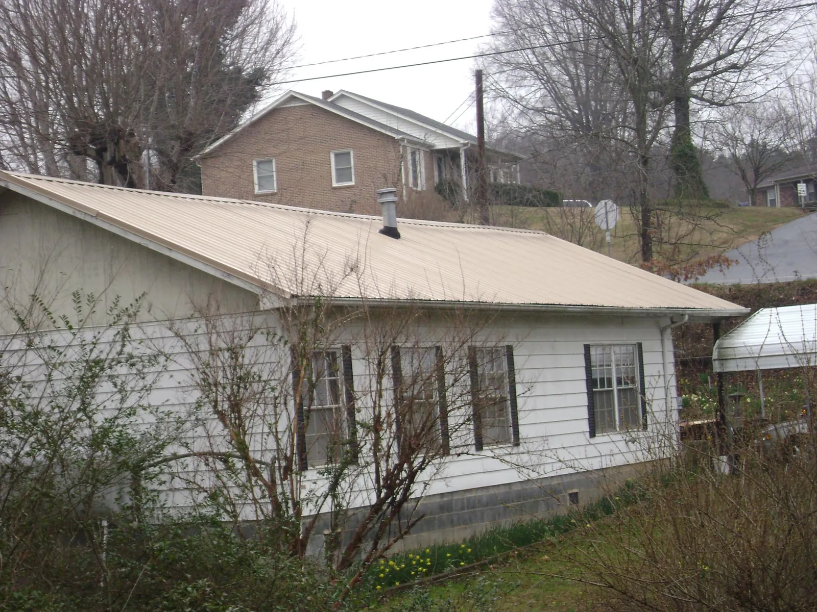 Tan metal roof on a white sided house set into a hillside — Commercial Roofing by Roofing Brothers in Etna